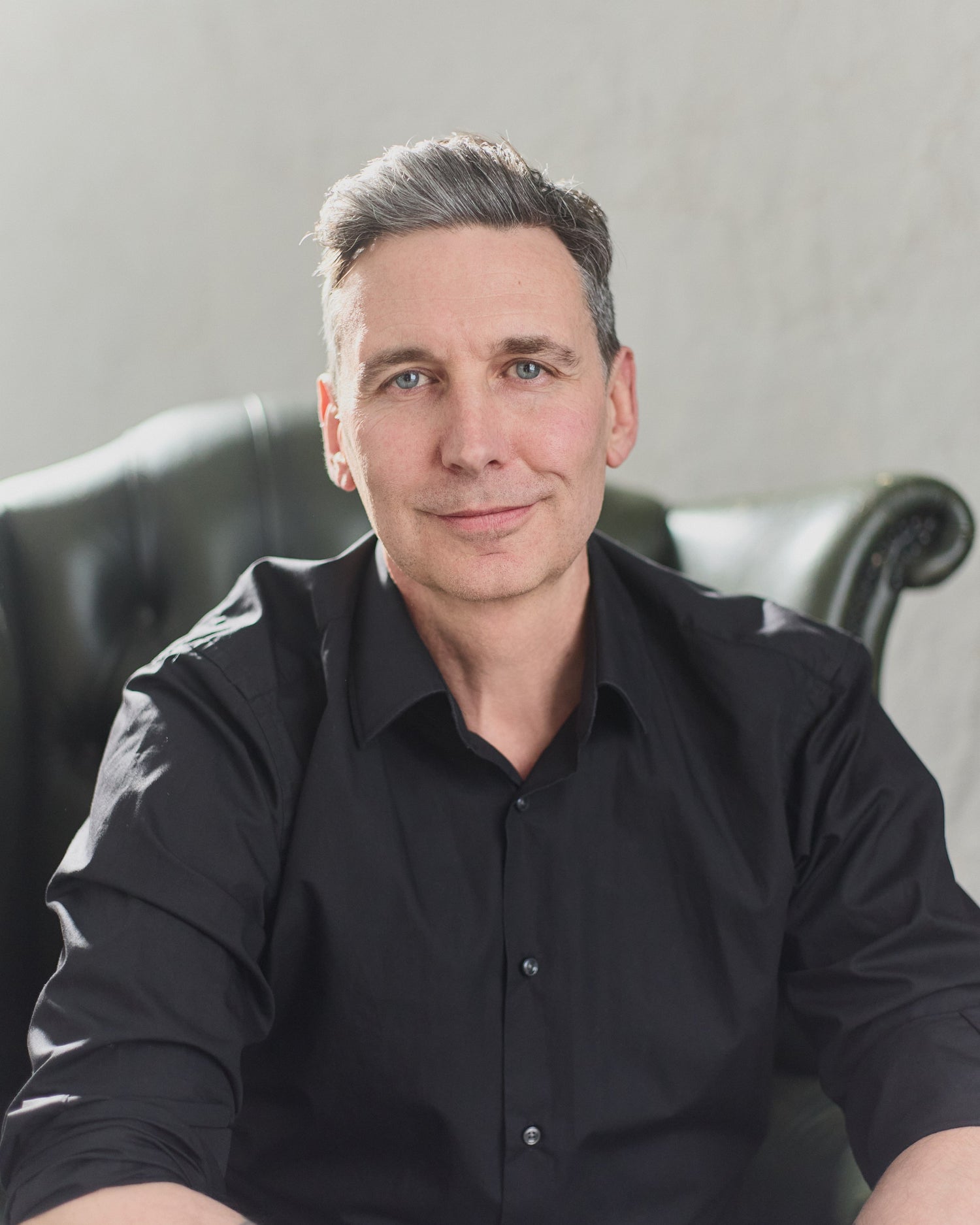 Image of Neil Sunley smiling sitting in a green therapists chair with a white background