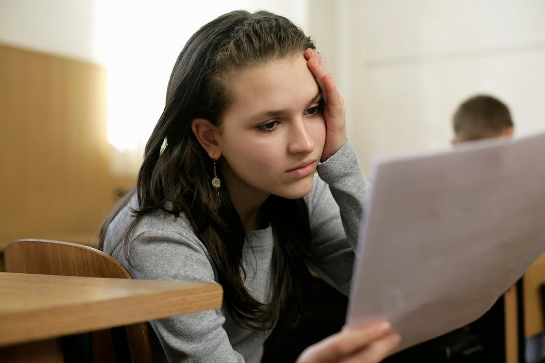 Teen girl looking stressed while reading a paper in a classroom, representing exam stress and anxiety.