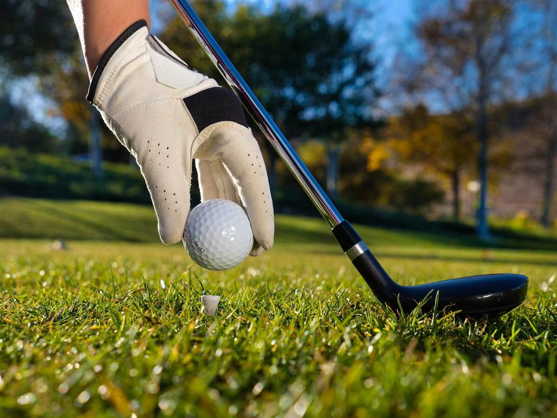 Golfer placing a ball on a tee with gloved hand, preparing for a focused drive on a sunny course
