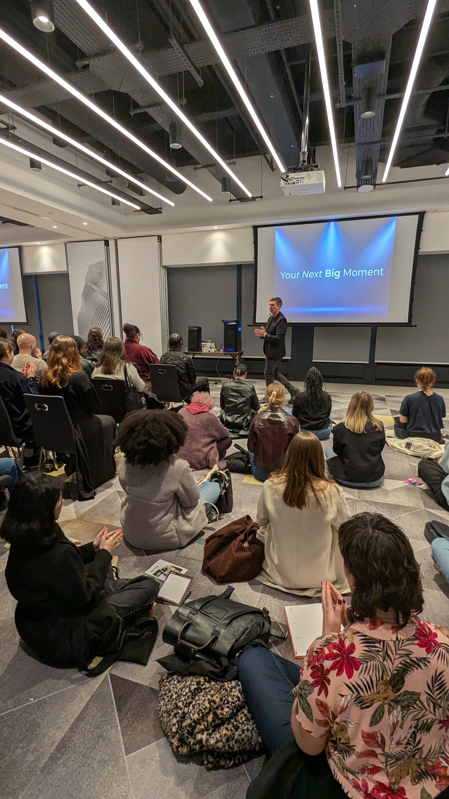 Neil Sunley giving a presentation to an audience in a modern conference room.